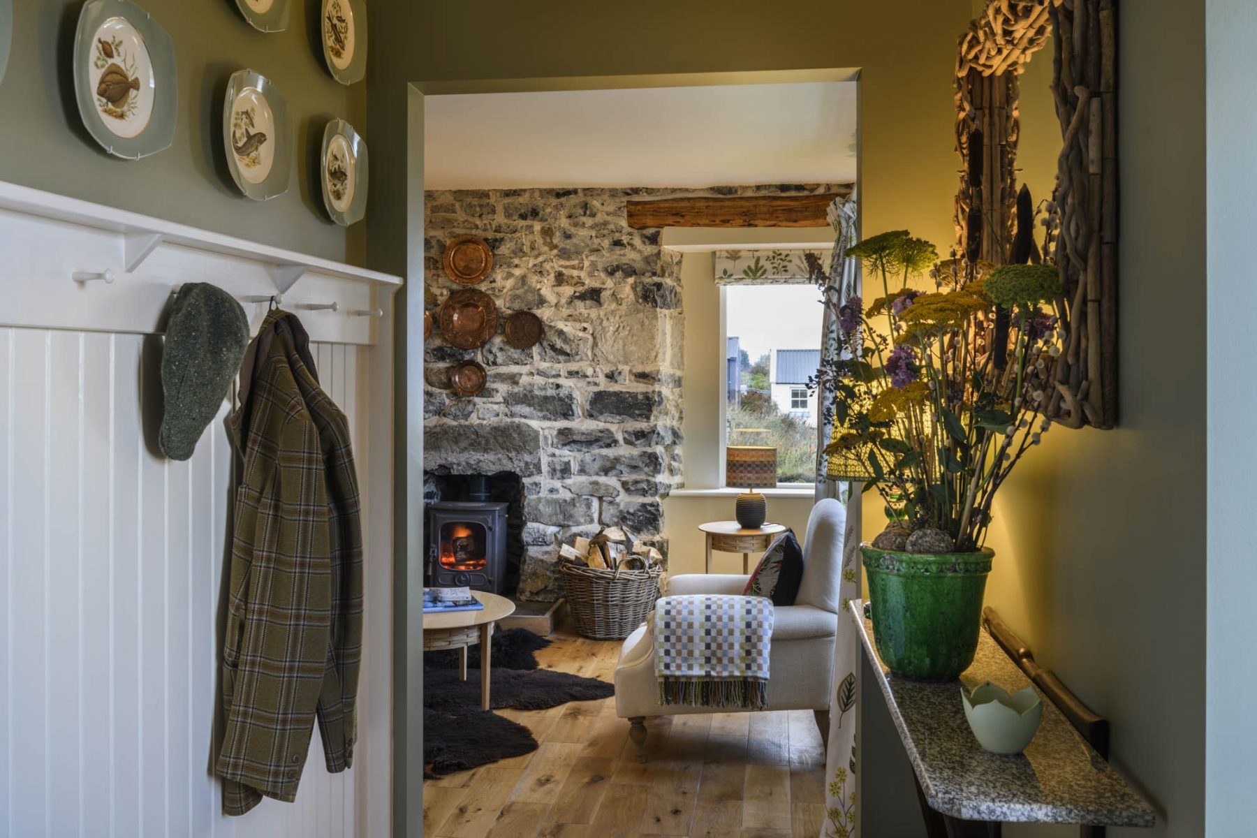 A Skye Croft House, looking down the hall past tongue and groove peg board to a cosy parlour with woodburning stove and with exposed stone walls.