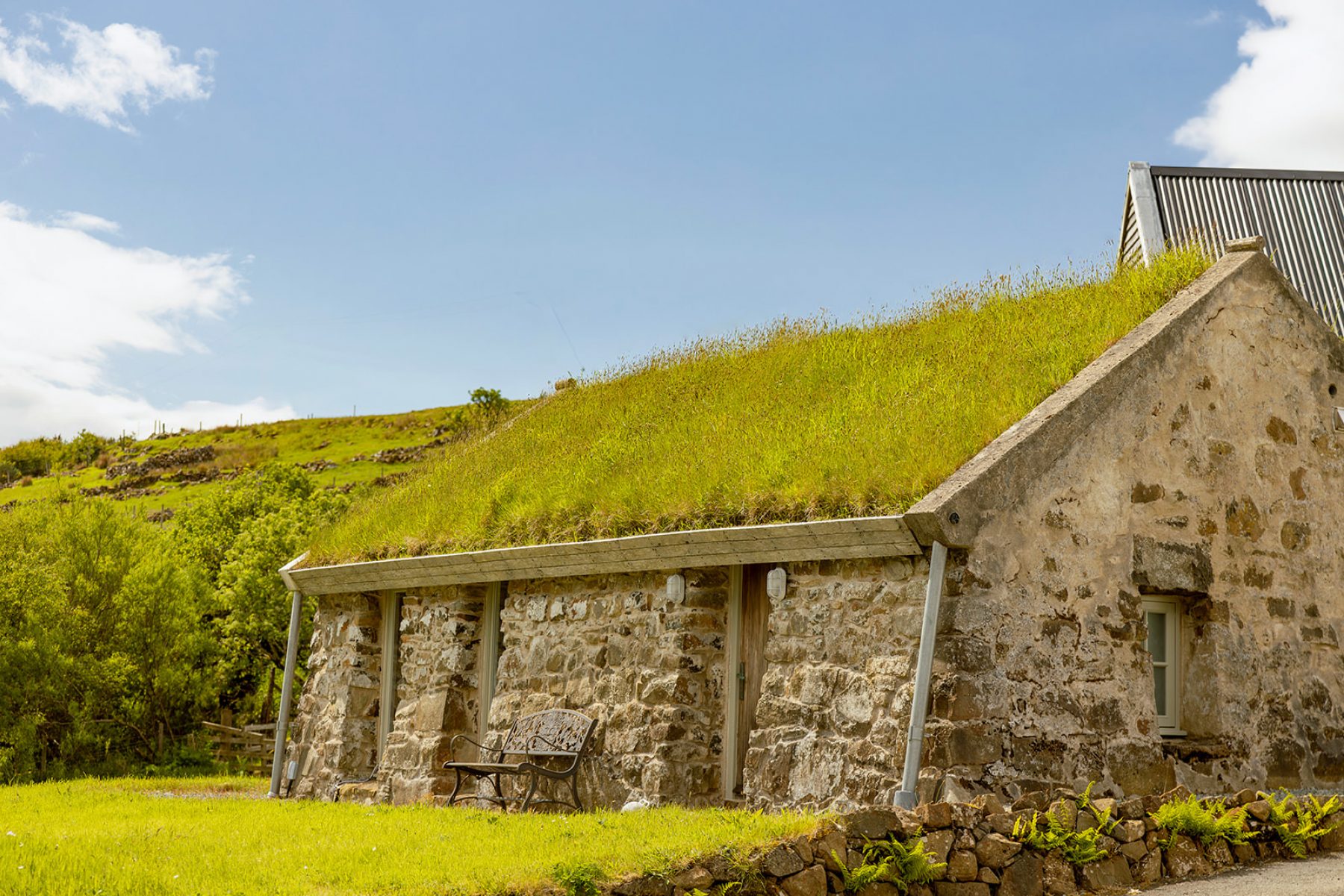 Traditional blackhouse cottage at Mint Croft Skye. A green grass roof on the low, single storey stone building with a grassy front garden.