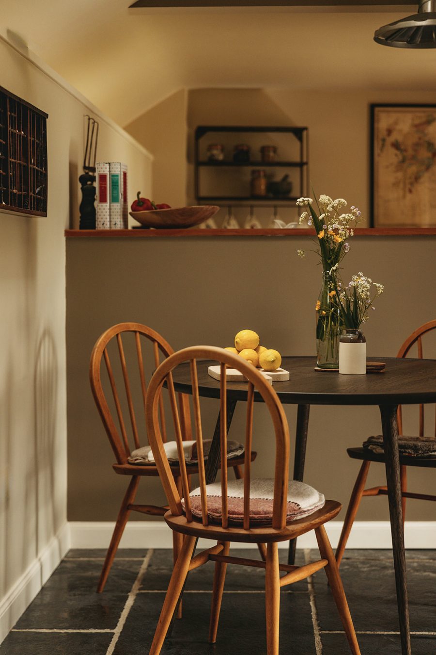 In the dining area at Mint Croft's historic blackhouse cottage in Skye. Spindle-backed chairs, a round wooden dining table and a view through to the open plan kitchen.