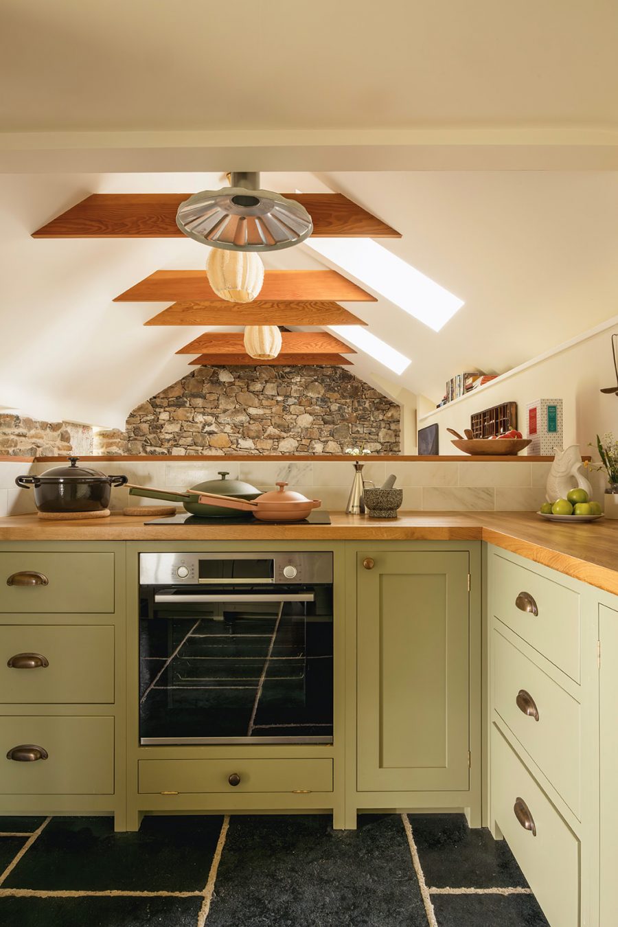 In the well-appointed open plan kitchen at the blackhouse cottage at Mint Croft, Skye. Handmade wooden kitchen with a view through to exposed rafters and stone wall in the open plan sitting room and dining area.