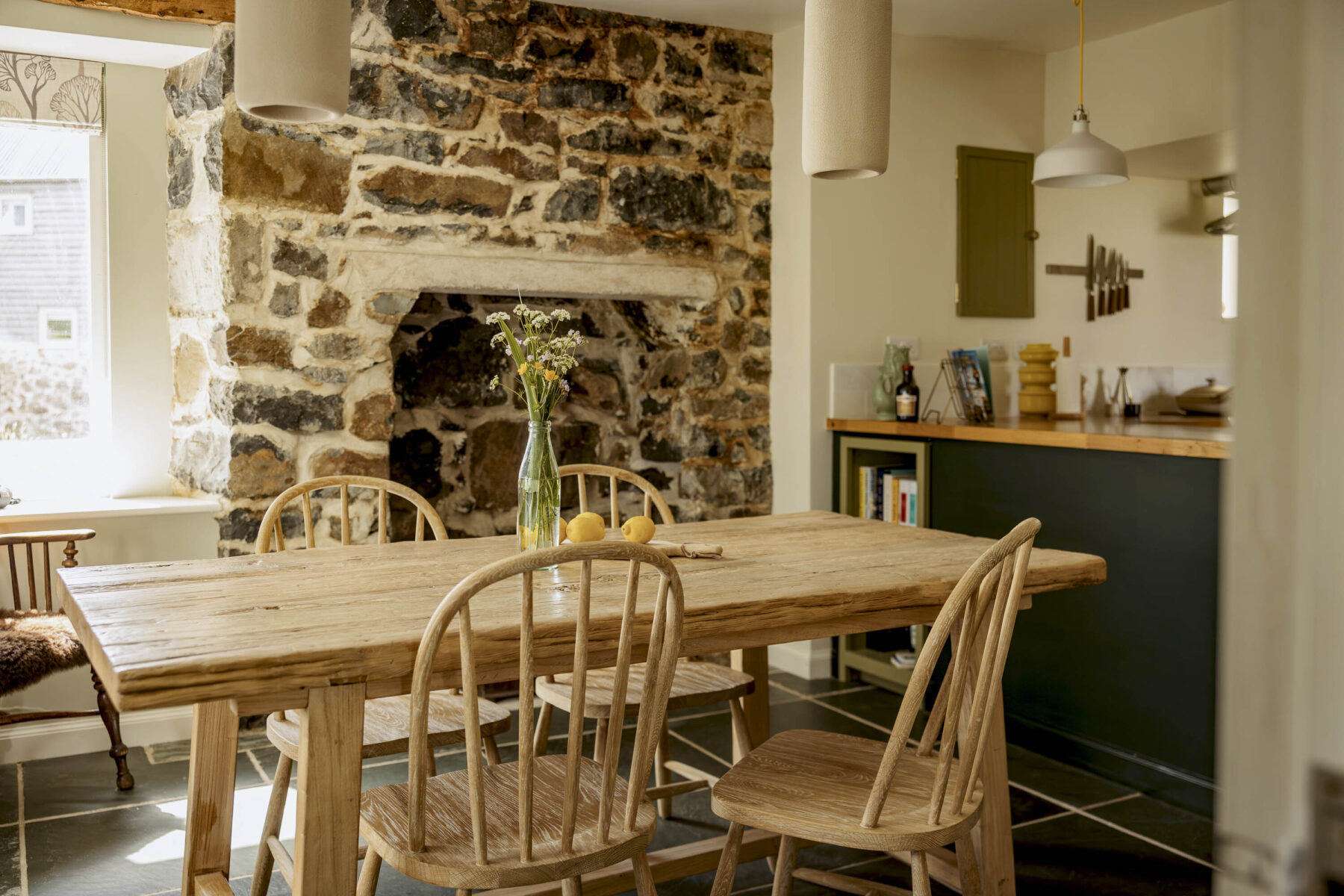 The kitchen table at Mint Croft's Croft House cottage. A wooden table and chairs by the exposed stone chimney brest and fireplace. At Geary, Skye, Highlands, Scotland.