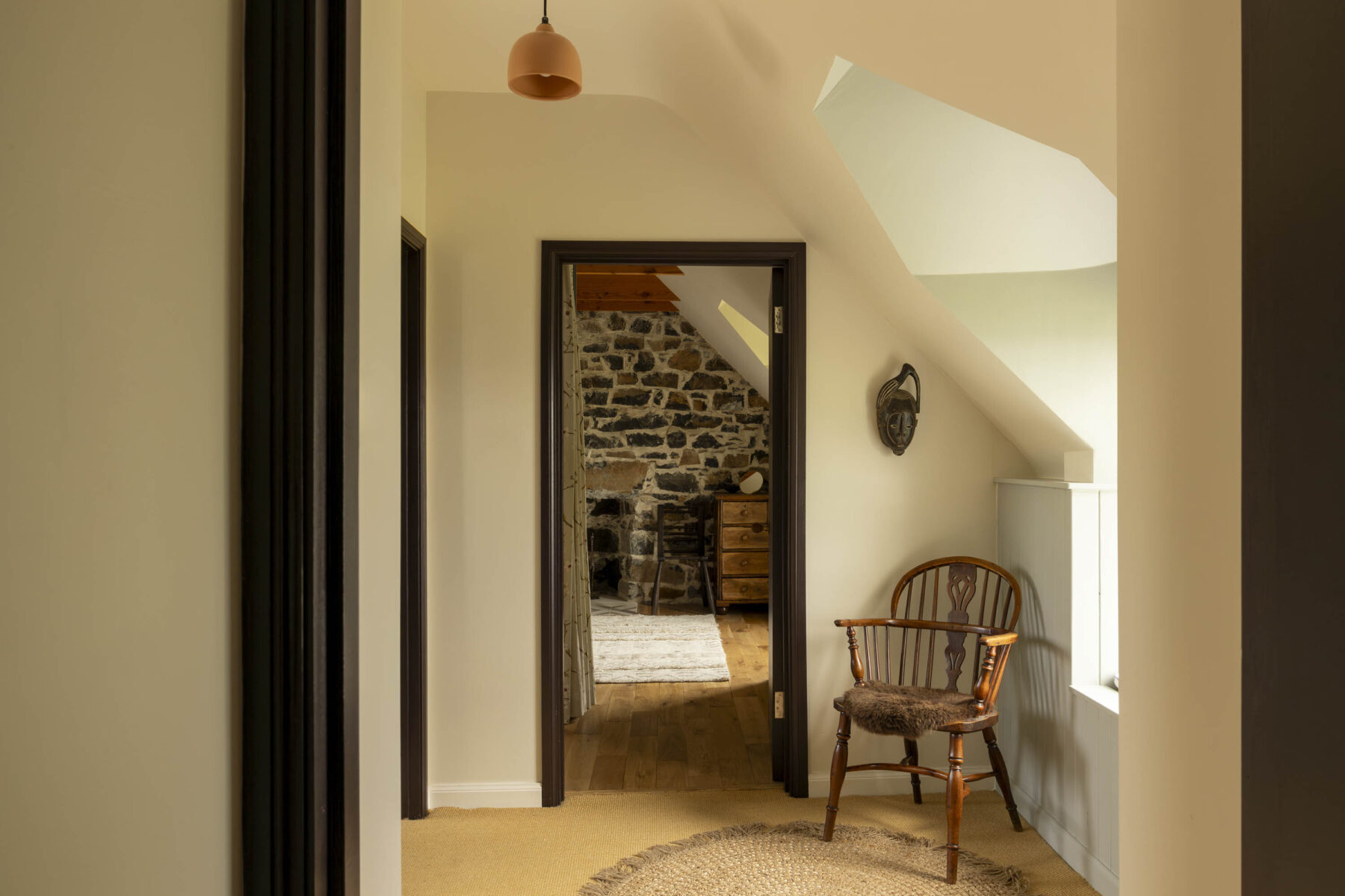 Upstairs inside a traditional Hebridean Croft House. A view through from one bedroom across a landing and into another bedroom with exposed stone wall.