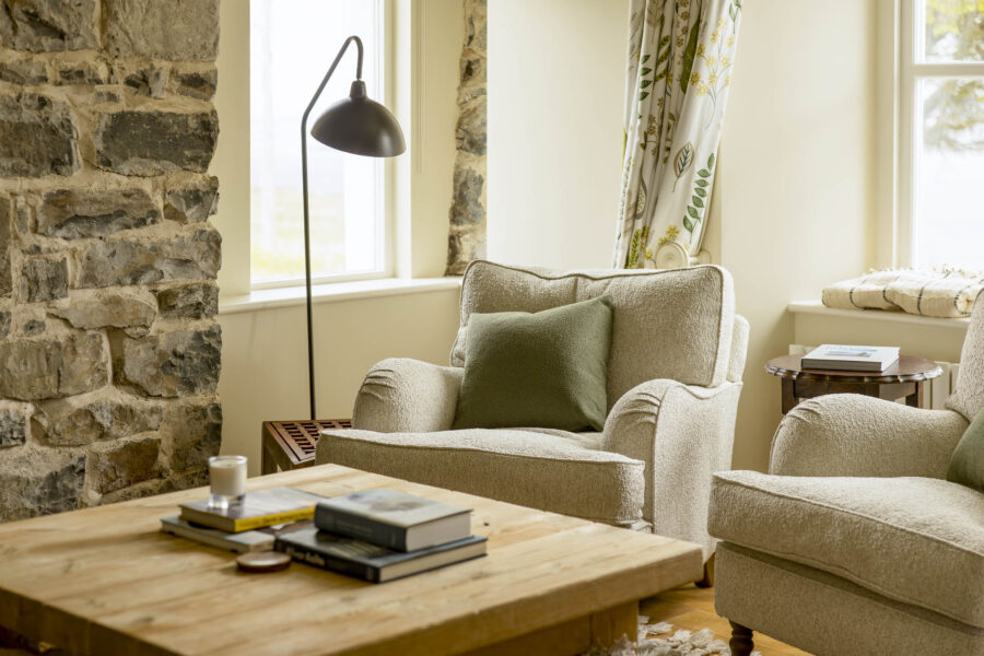 In the sitting room in the contemporary interiors of the traditional stone croft house cottage at Mint Croft, Skye, Scottish Highlands. Comfortable armchairs upholstered in pale fabric, wooden coffee table, exposed stone chimney breast.