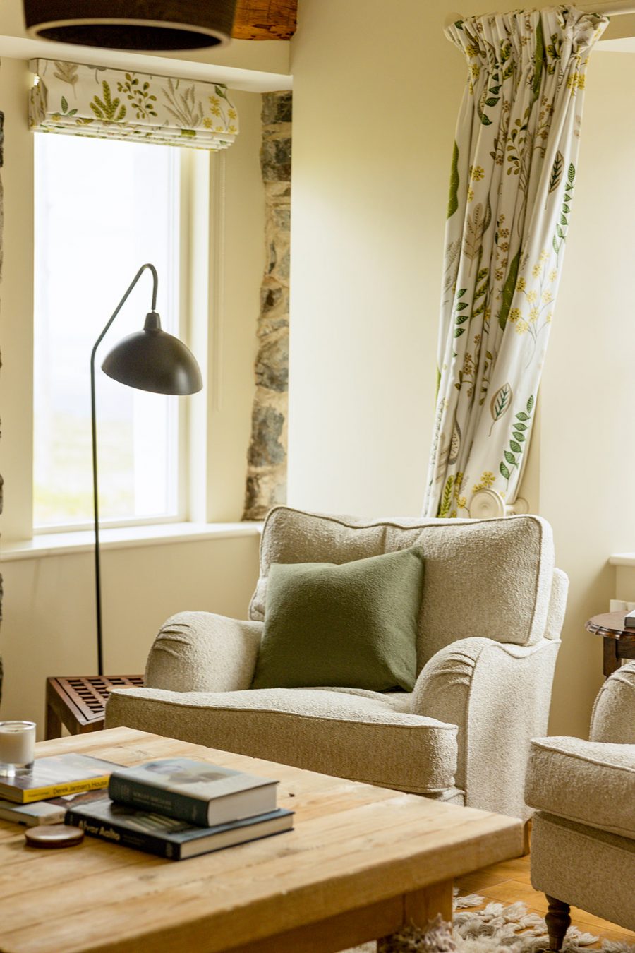 In the sitting room at the Croft House, Mint Croft luxury holiday cottages, Isle of Skye. Comfortable armchairs in pale neutral upholstery, wooden coffee table, curtains and blinds in soft colours.