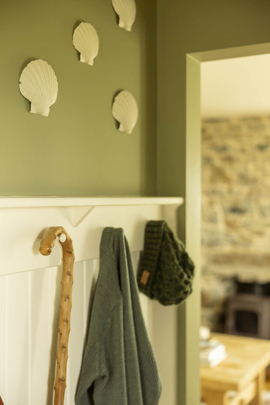 In the front hall at the croft house at Mint Croft, Isle of Skye. Sage green walls with white panelling and peg coat rack. Scallop shells hung on the wall.