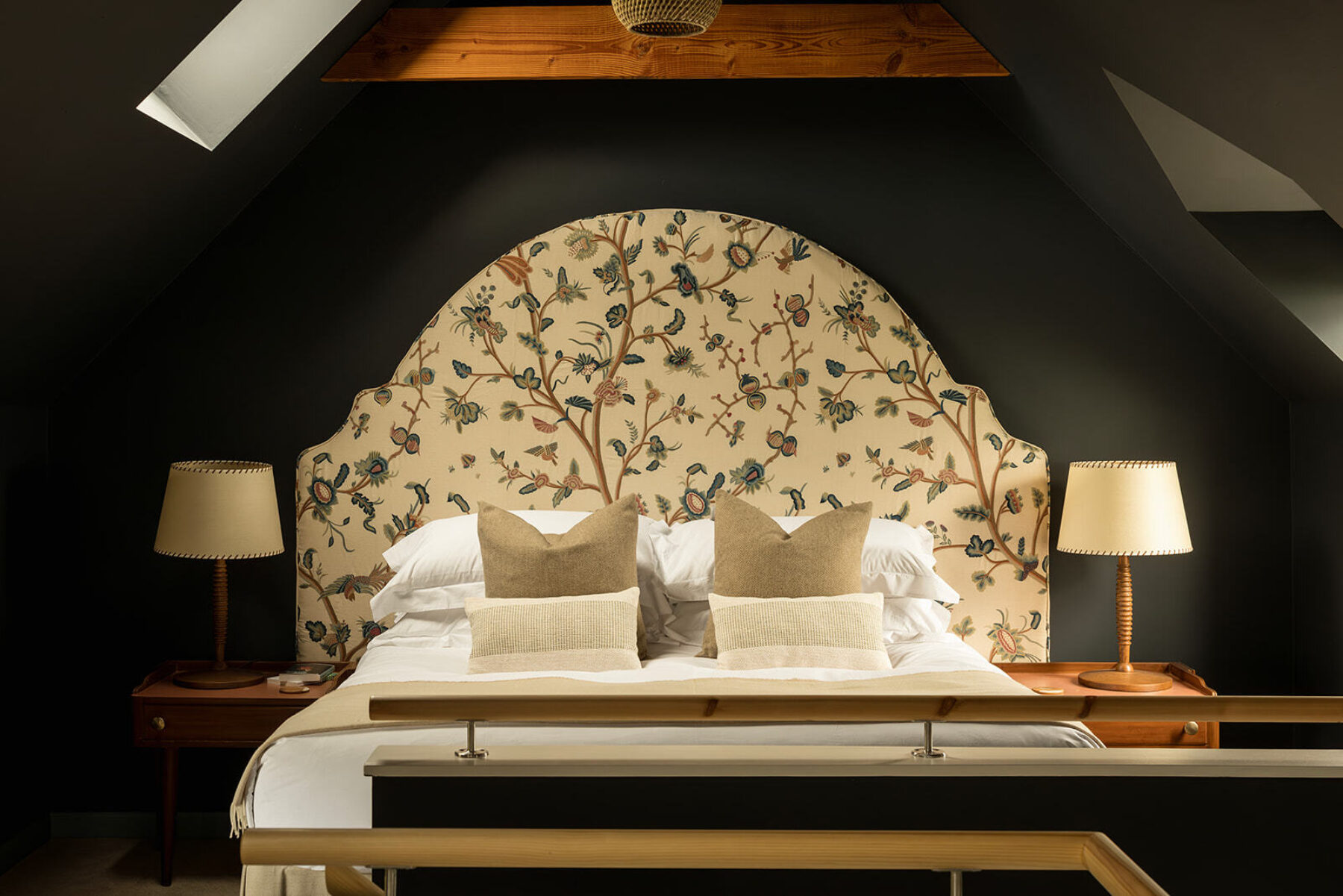 The bedroom at the blackhouse cottage, luxury accommodation within a traditional stone croft building in the Isle of Skye, Scotland. Exposed rafters, dark atmospheric walls and an crewel work, upholstered headboard in this luxury cottage for two.