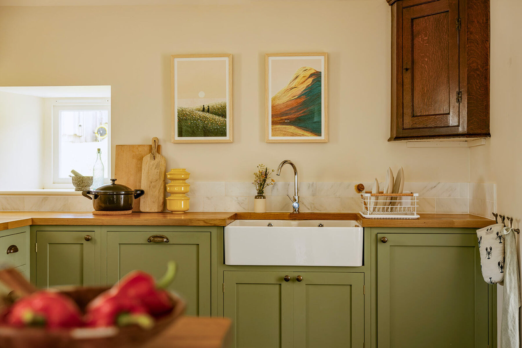 Croft House kitchen at Mint Croft, Skye, a traditional Higland cottage. Wooden green-painted kitchen with wooden worktop, framed artwork, pans and cookware. Antique wooden corner cupboard mounted on the wall.