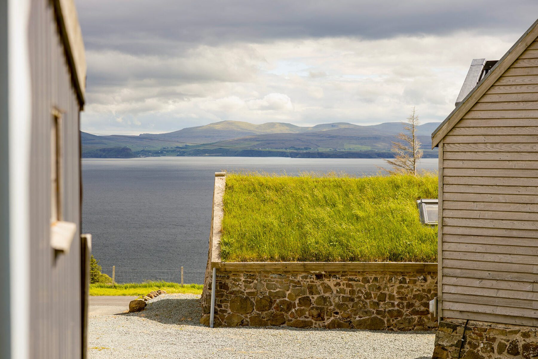 Cluster of cottages at Mint Croft, Skye, including a hebridean blackhouse cottage with traditional green roof of grasses. Beyond, a view across the sea to Trotternish.