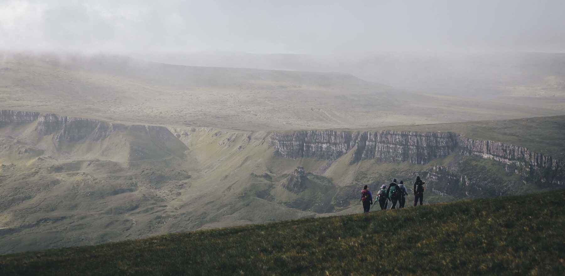 Hillwalking on the Isle of Skye, Scotland. A small group of walkers on a hill with a hazy view looking across moorland and cliffs