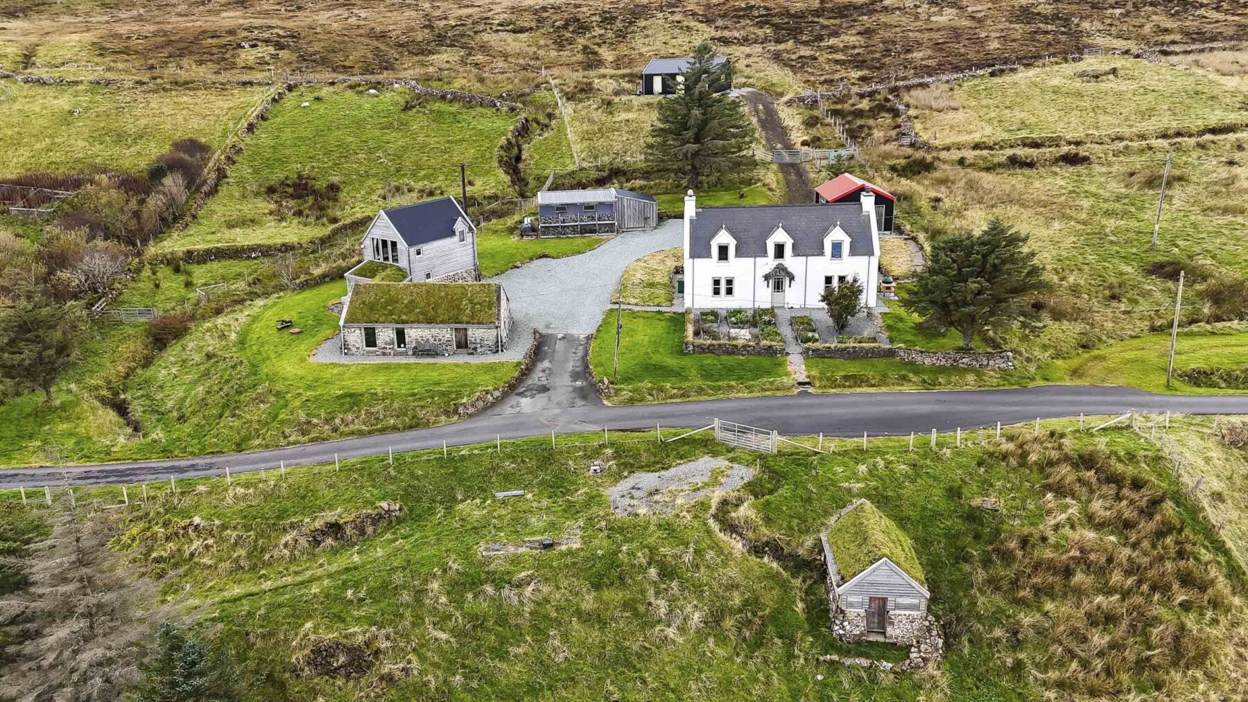 Aerial view of Mint Croft. A collection of small and traditional buildings including a restored hebridean blackhouse cottage and whitewashed stone croft house. Set in croft land and moorland at Geary, Isle of Skye, Scottish Highlands.