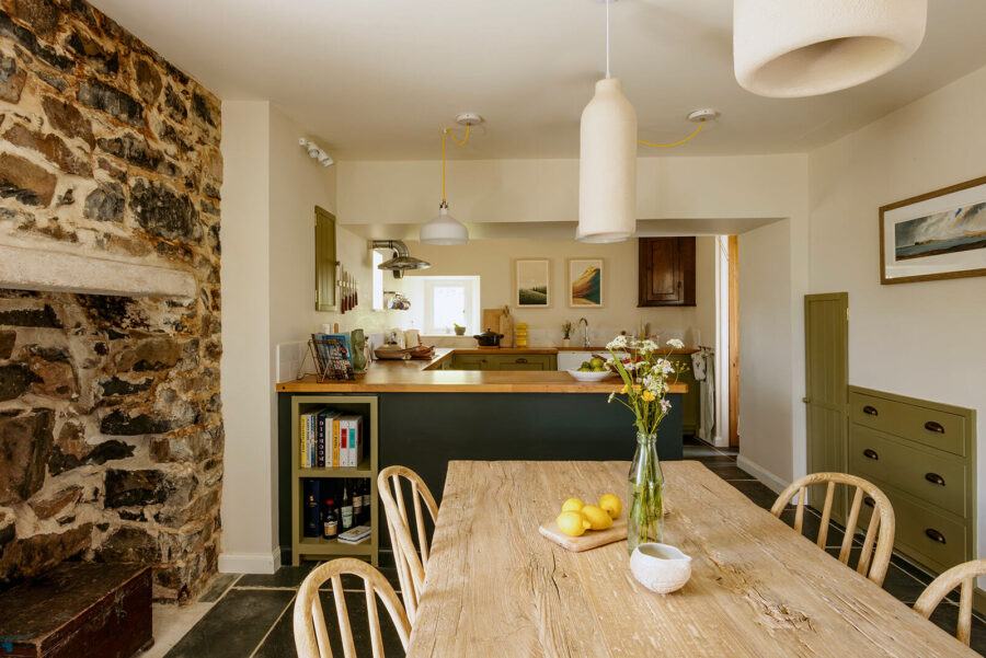 In the kitchen at a traditional stone cottage in the Isle of Skye, Scotland.  Exposed stone chimney breast, wooden kitchen table and chairs, contemporary wooden kitchen