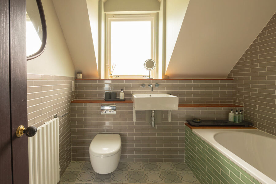 Spacious bathroom with fired earth metro tiles in grey and green. Large bath, WC, sink.