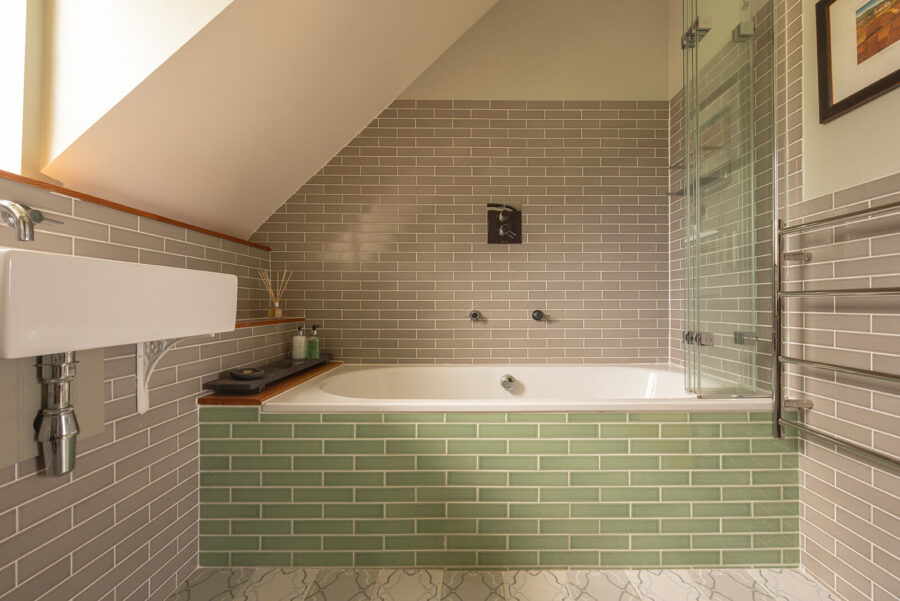 Double ended bath in cottage bathroom with grey and green metro tiles by Fired Earth