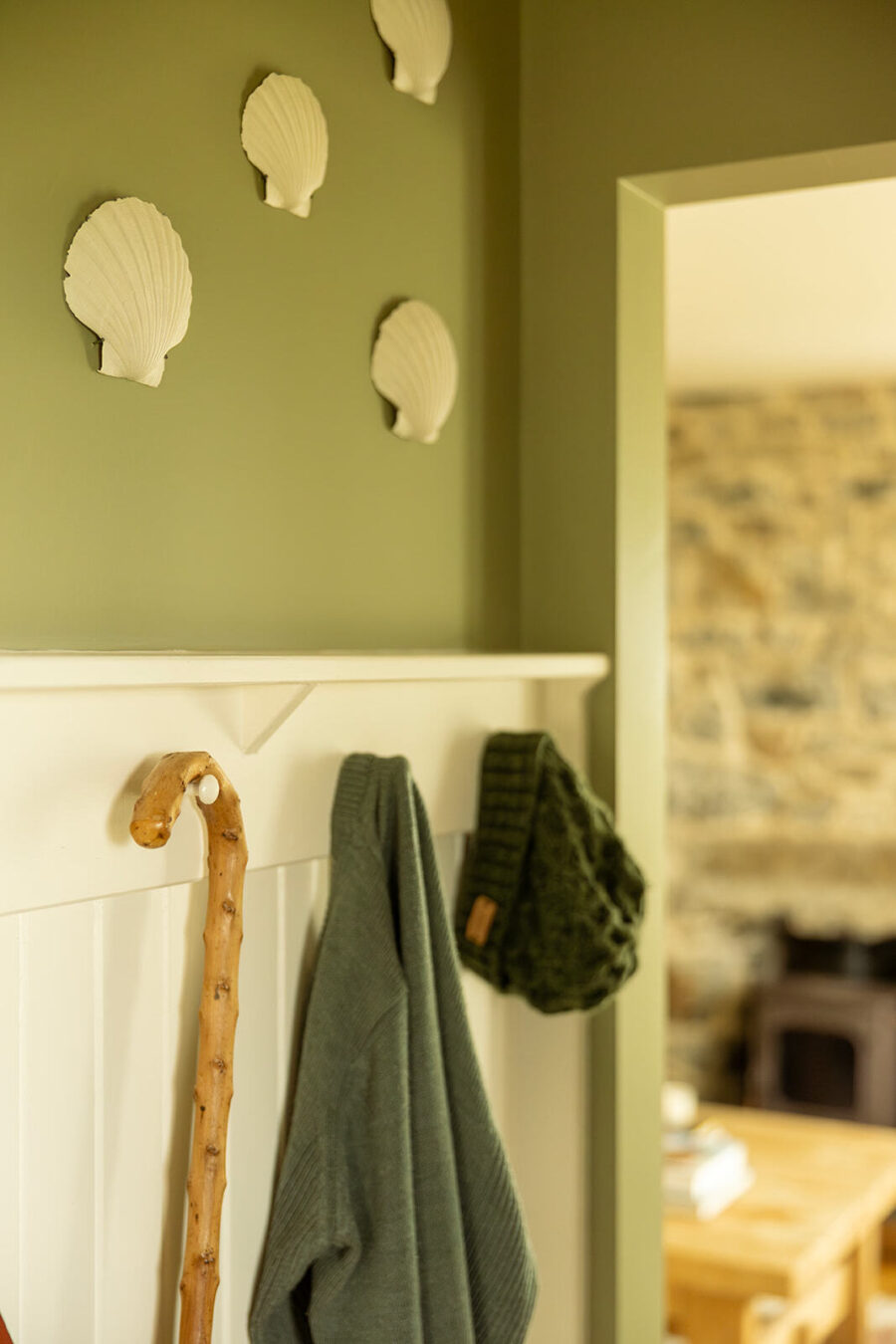 White tongue and groove panelling with coat pegs in the hall at Mint Croft's croft house cottage. Above, on sage green walls scallop shells are mounted.