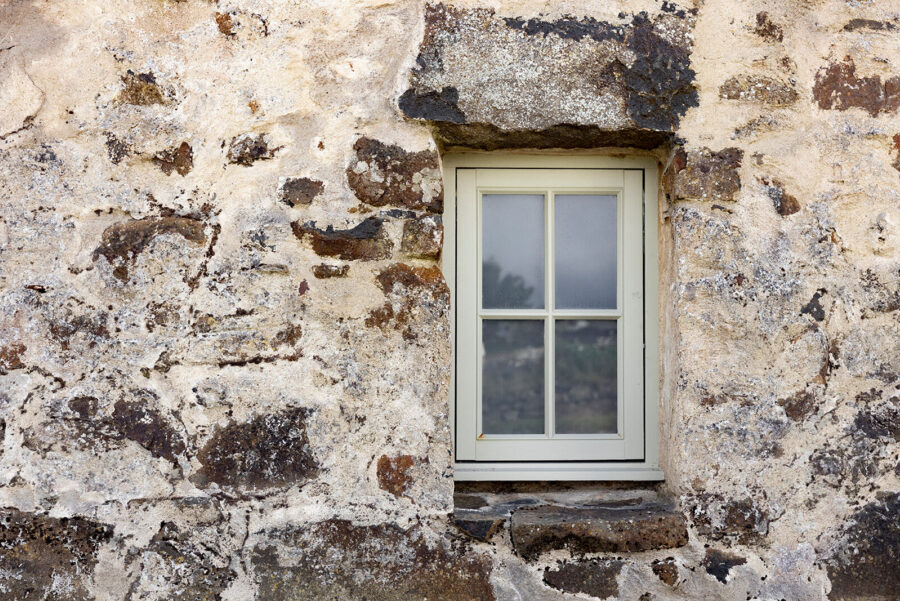 Small traditional wood-framed window at the Blackhouse cottage, Geary, Waternish, Isle of Skye. Painted soft green and set into a stone wall with traditional render.