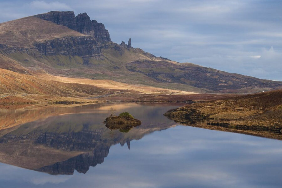 The Old Man of Storr, Trotternish, Skye, Scotland. A tall rock formation beneath cliffs, reflected in a small loch.